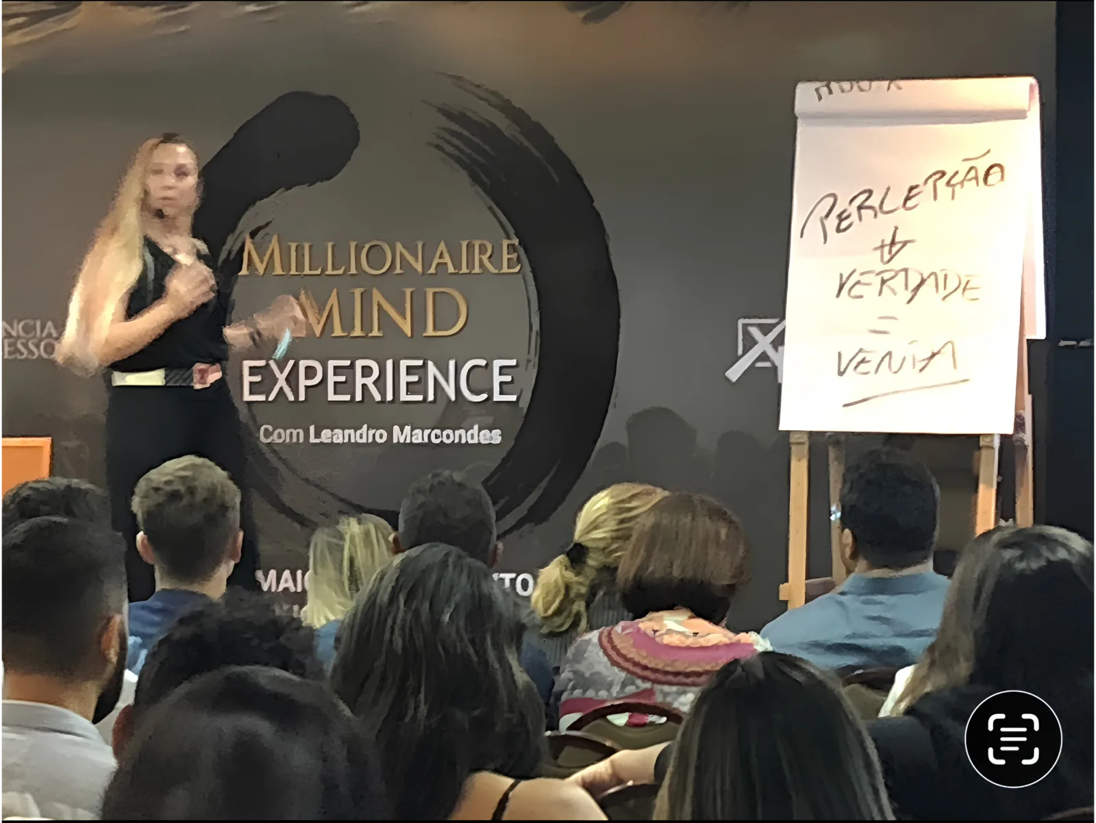 Pilar Moretzsohn fala no palco ao lado de um flip chart.