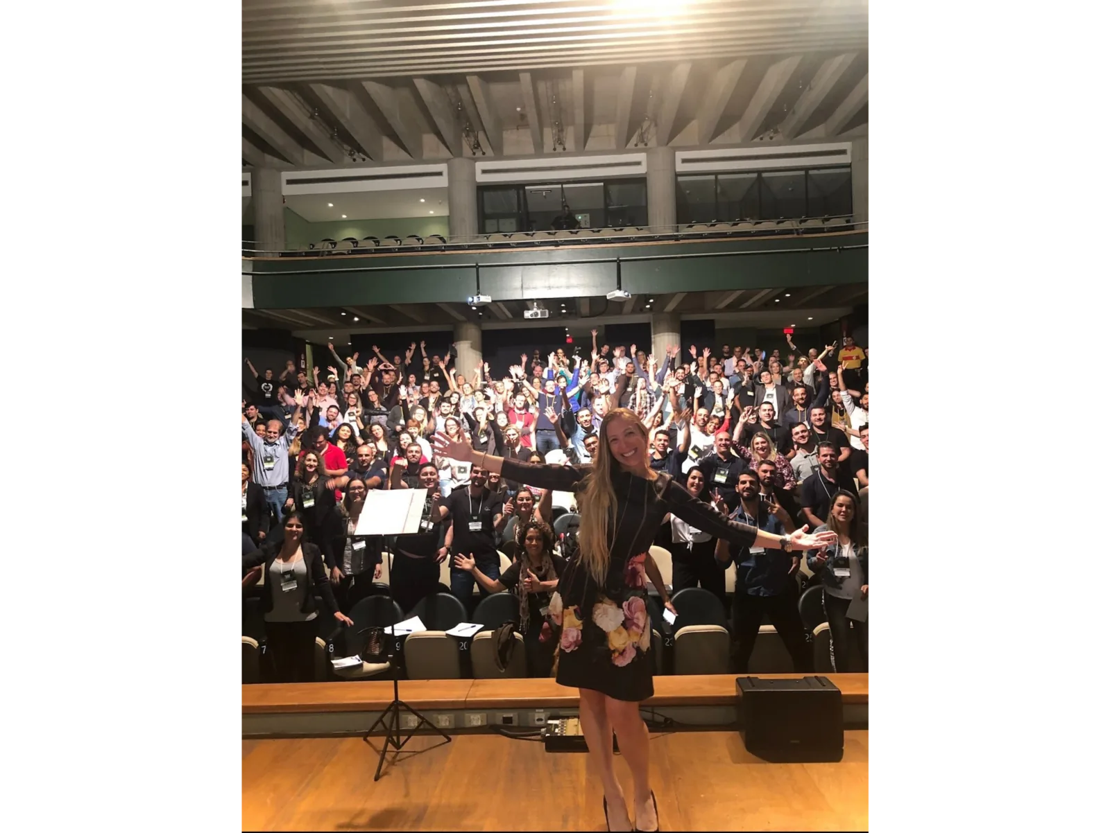 Pilar Moretzsohn abre os braços no palco diante de uma plateia em auditório.